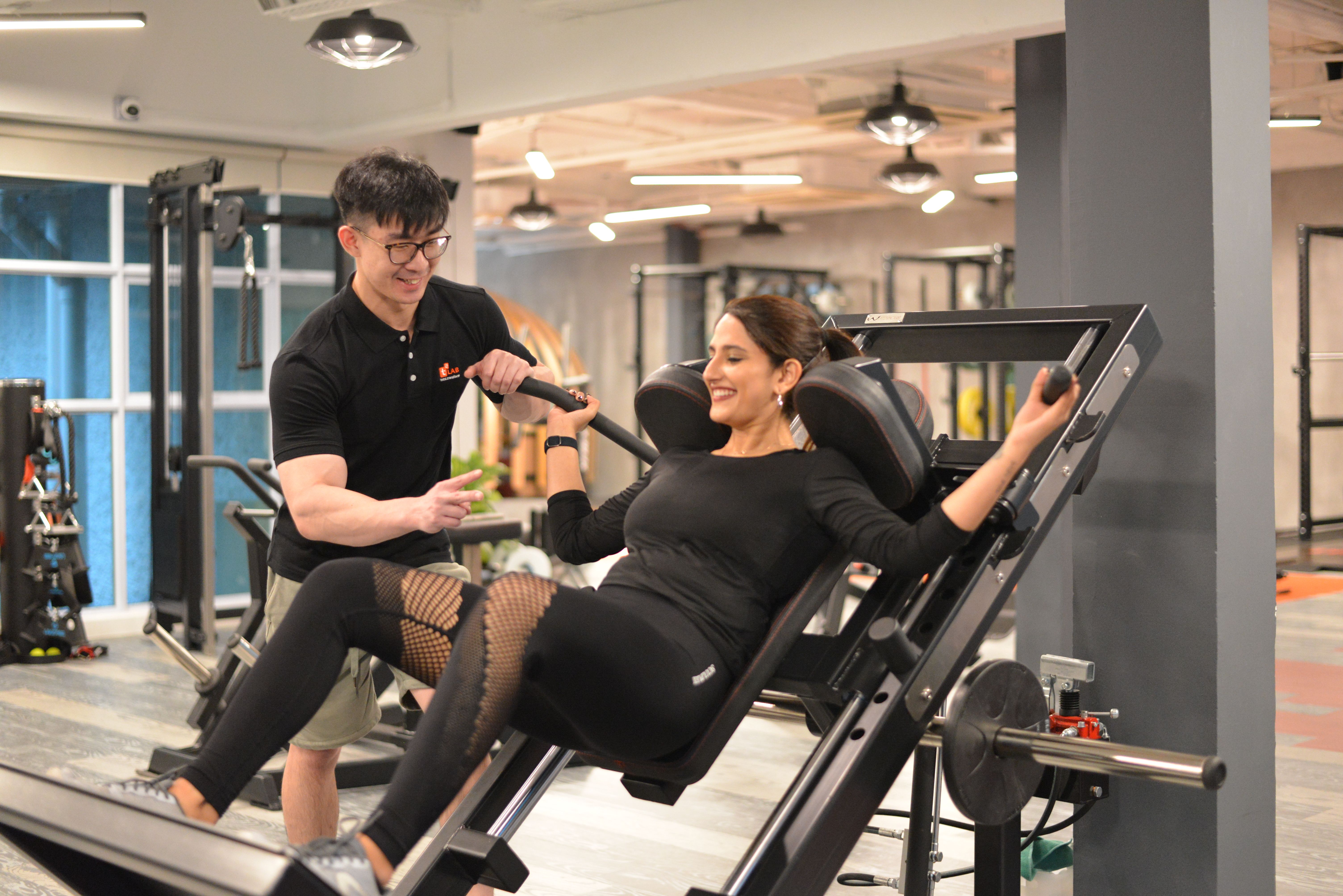 Trainer coaching a client on a leg-press machine